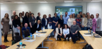 Picture of partners who met in Waterford. A group of 30 people with more participants joining online on the screen behind them.