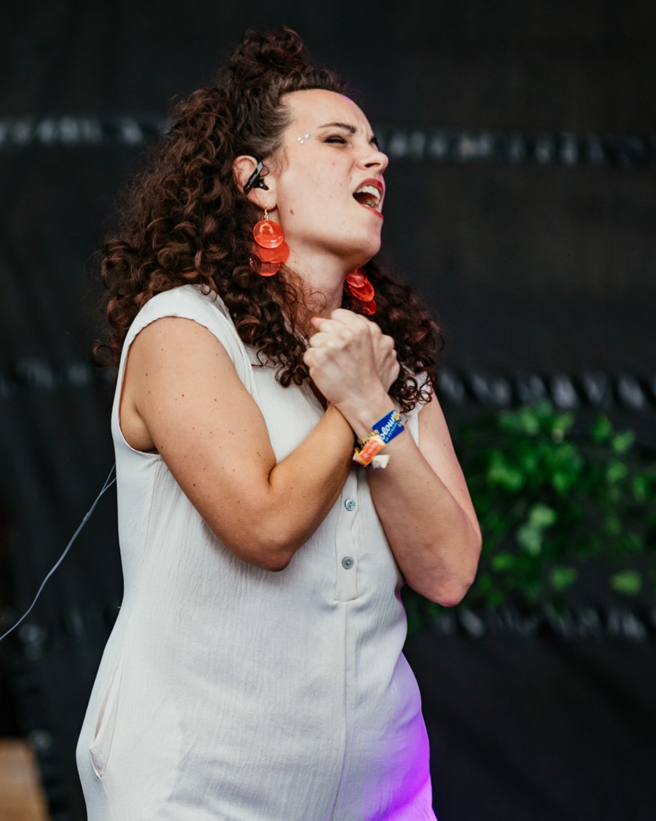 A sign language interpreter clasps her hands to her chest on stage at the Colours of Ostrava festival. She is wearing a white sleeveless dress and red earrings.