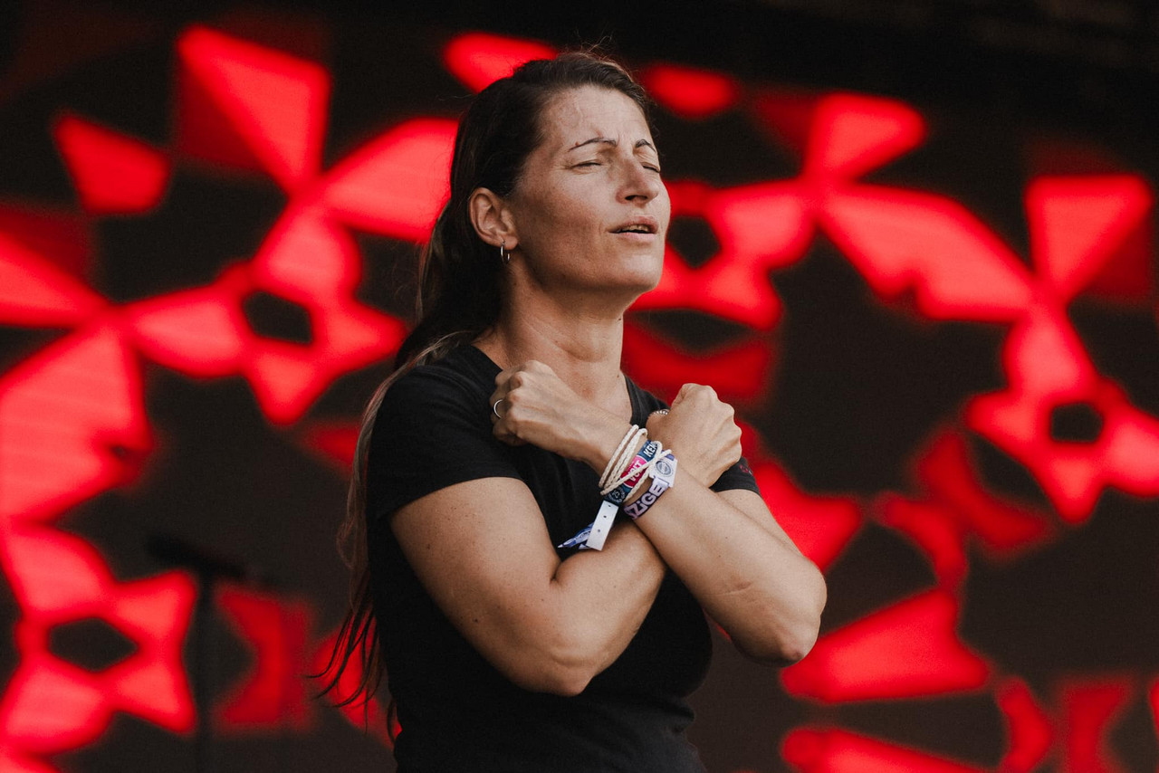 Sign language interpreter at Sziget festival closes her eyes on stage and crosses her arms against her chest. Her long brown hair is in a pony tail and she is wearing a black t-shirt.