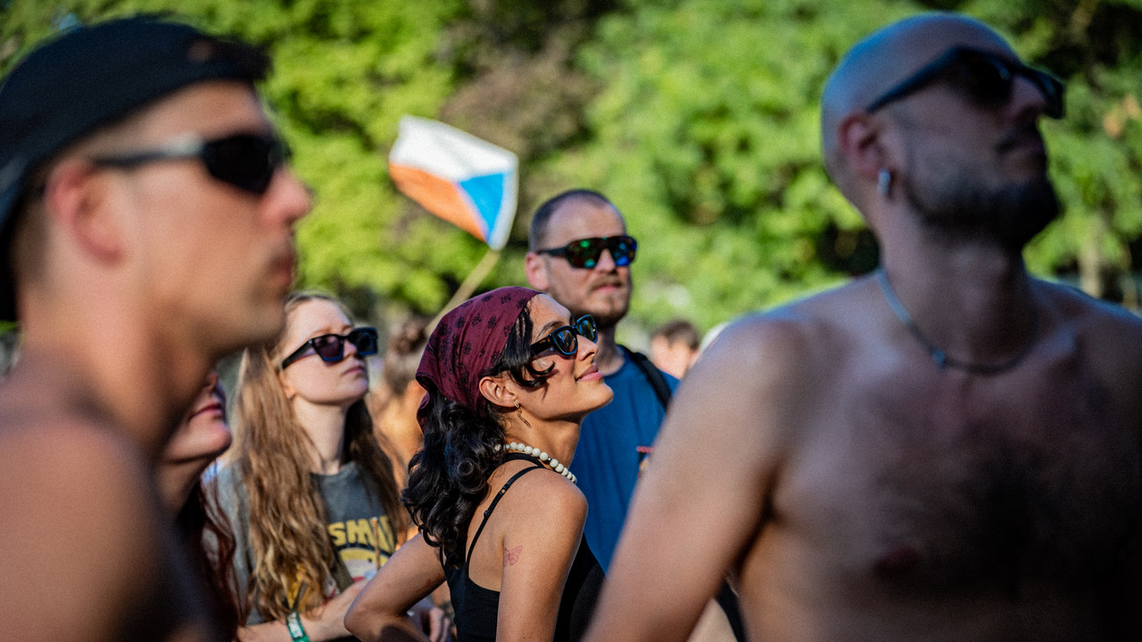 Sziget festival goers dance to the music in an outdoor space. A woman with a bandana and sunglasses is in the centre while other young adults are dancing around her.