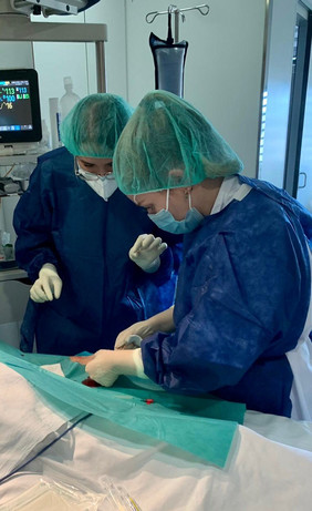 Image of Clàudia Ferragut López and another nurse assisting in surgery they are wearing full scrubs and tending to a patient