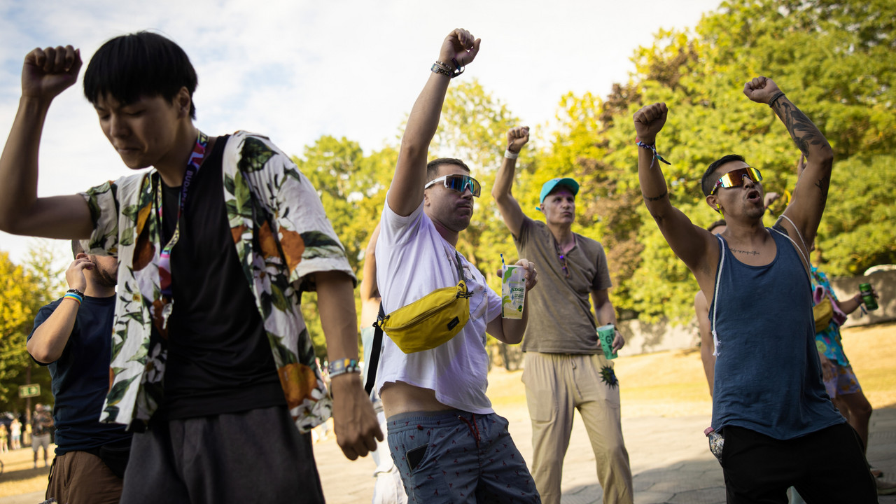 Four young adults put their hands in the air and dance to the festival music outdoors.