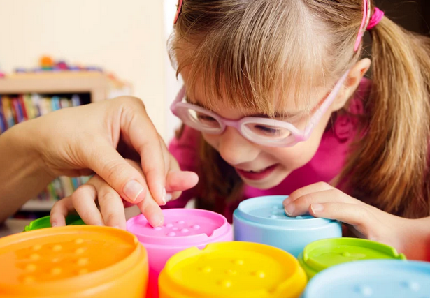 Picuture of a young girl with a disability in school, learning. She is playing with coloured cubes, and smiling. 
